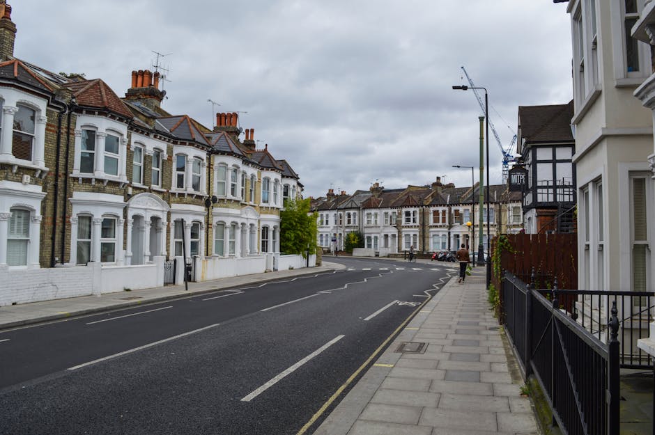 A quiet residential street in Earls Court with traditional Victorian terraced houses featuring decorative mouldings, bay windows, and brick facades painted in white and neutral tones. The pavement is 